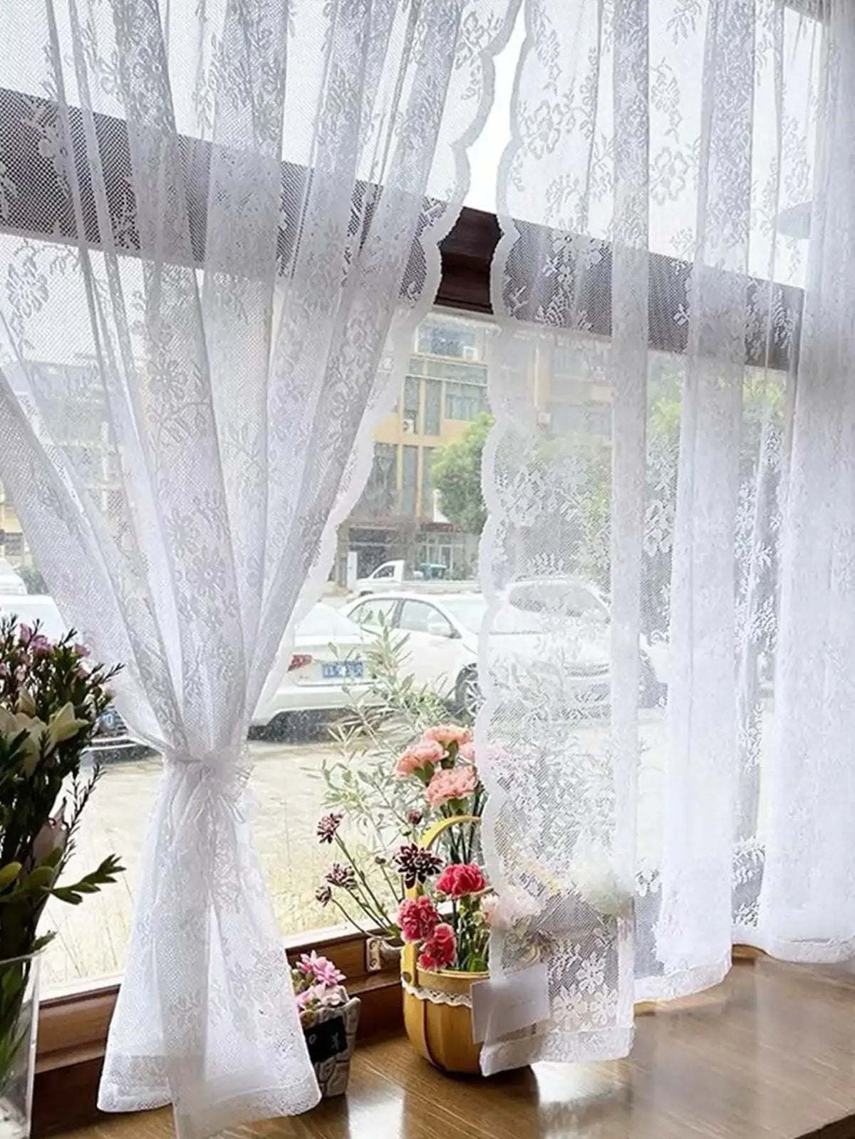 Rideau transparent avec broderie florale blanche, suspendu à une fenêtre avec vue floue extérieure