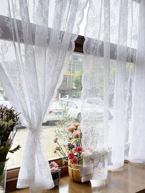 Rideau transparent avec broderie florale blanche, suspendu à une fenêtre avec vue floue extérieure