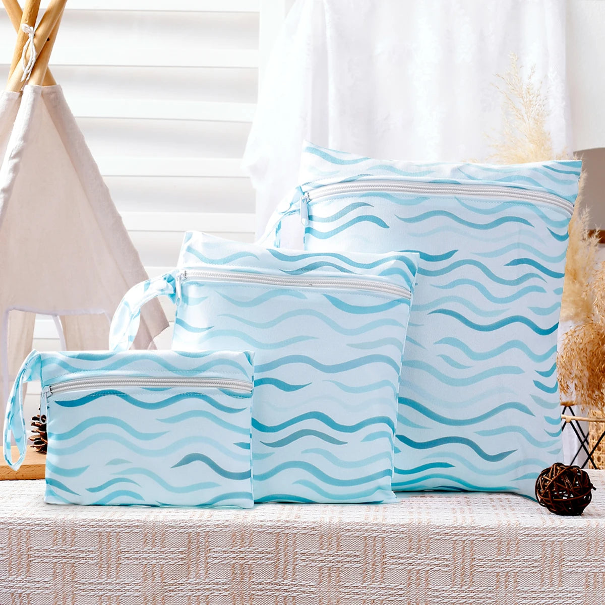 A set of light blue reusable waterproof wet bags with a wavy pattern displayed on a table.