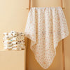 A white patterned soft cotton gauze baby swaddle blanket hanging on a wooden rack.