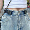 A close-up of a woman wearing a white top and light wash denim skirt with a black leather belt and chain strap.