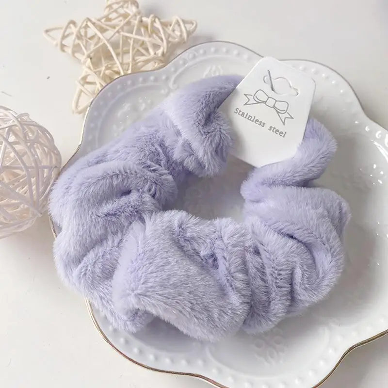 A close-up of a lavender plush coil hair tie made of soft faux fur resting on a white plate.