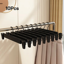A set of ten black adjustable clip hangers hanging from a metal rod, used for storing pants and skirts.