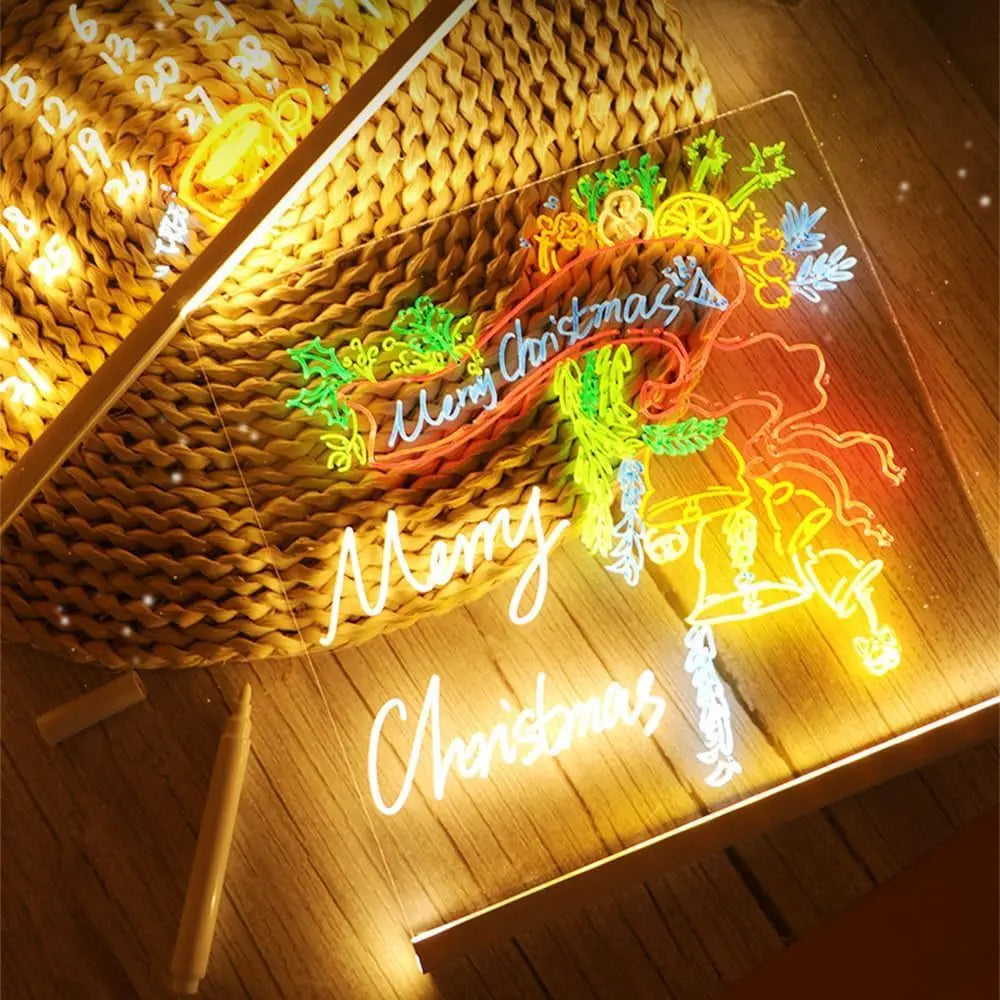 An LED drawing board with seven pens and a night light illuminating Christmas-themed drawings on a wooden surface.