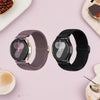 A close-up of a purple braided nylon watch band and a black watch with a silver clasp on a pink background.
