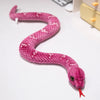 A pink, textured lifelike snake plush toy resembling an anaconda doll lying on a white surface.