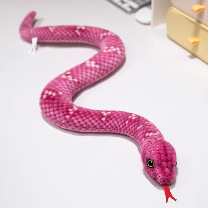 A pink, textured lifelike snake plush toy resembling an anaconda doll lying on a white surface.