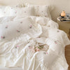 White duvet cover set with pink rose embroidery and lace details on a bed.