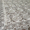 White lace tablecloth featuring an embroidered rose pattern on a wooden surface.