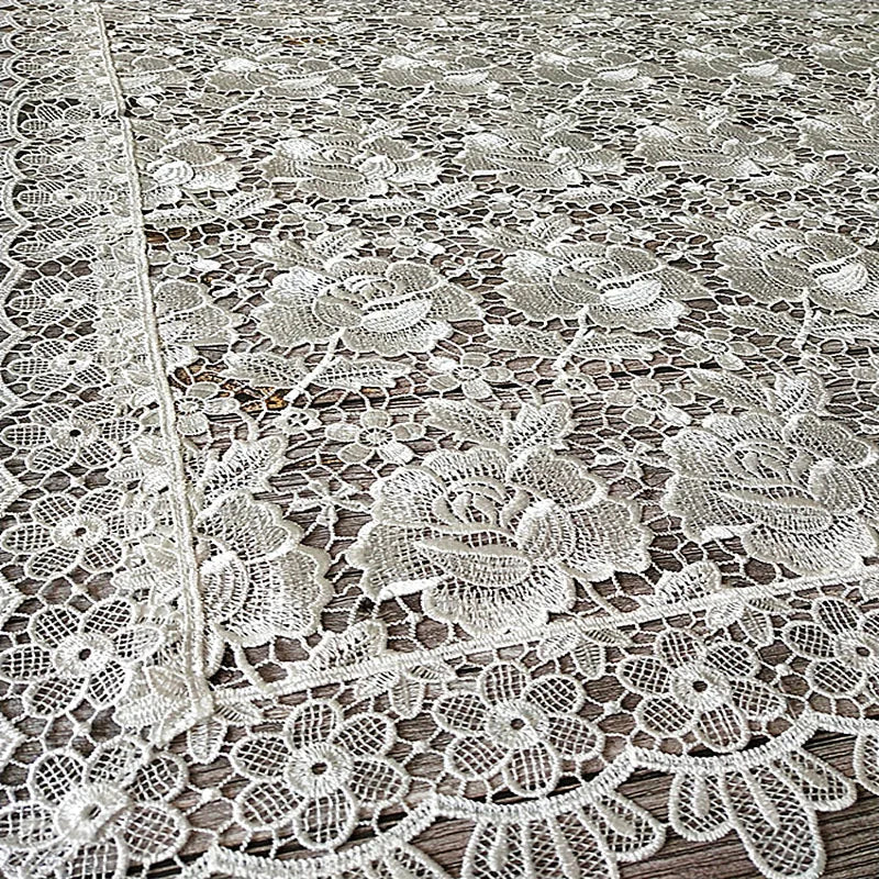 White lace tablecloth featuring an embroidered rose pattern on a wooden surface.