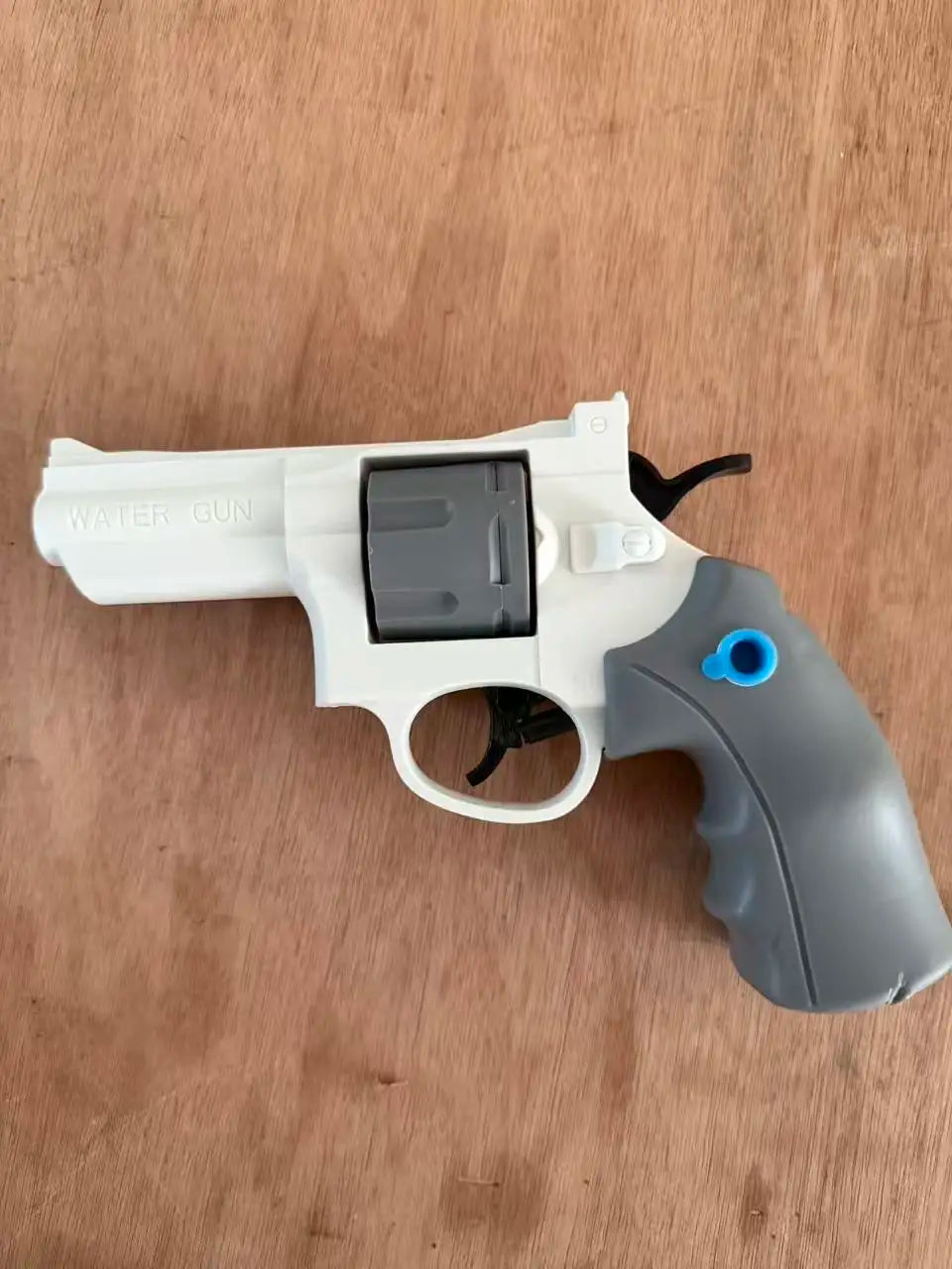 A white mini mechanical revolver water gun with a gray grip and a black chamber is shown on a wooden surface.