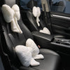 A black car interior showing a plush white bowknot headrest pillow with neck support placed on the seat.