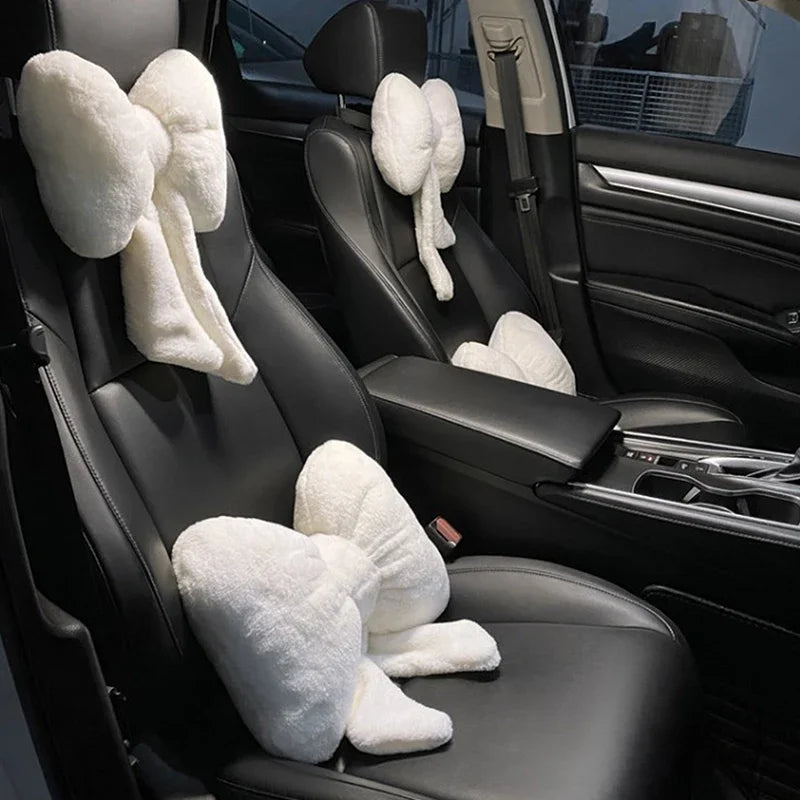 A black car interior showing a plush white bowknot headrest pillow with neck support placed on the seat.