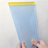 A clear blue pre-taped masking film is held by a hand, showing its translucent texture and yellow tape edge.