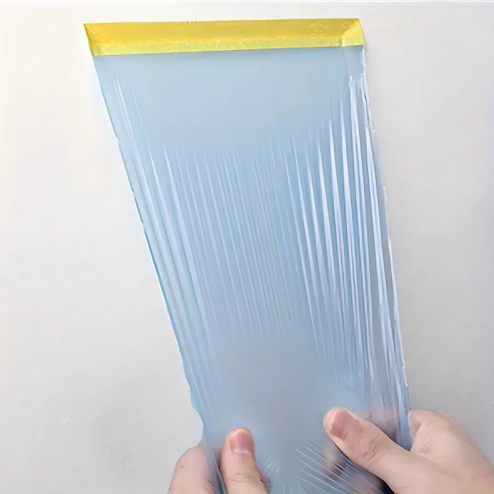 A clear blue pre-taped masking film is held by a hand, showing its translucent texture and yellow tape edge.