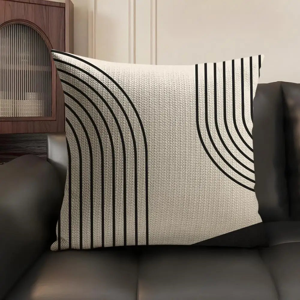 A beige linen cushion cover with black geometric lines is displayed on a dark leather sofa.
