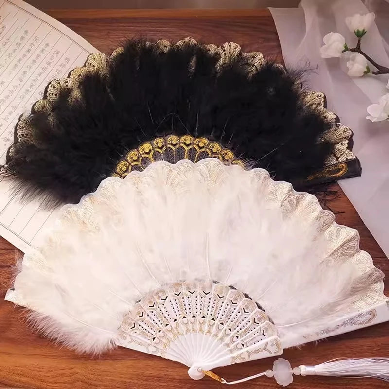 A vintage folding fan with a white lace-trimmed surface and a golden edge is displayed next to a black feather fan.