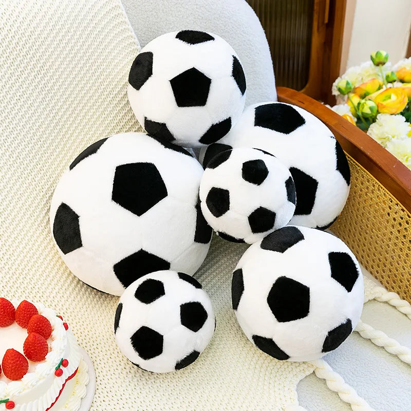 A collection of white and black football-patterned plush pillows resting on a light-colored fabric.