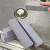 Several gray pumice stone cleaning sticks are displayed on a metal surface with a circular metal object.