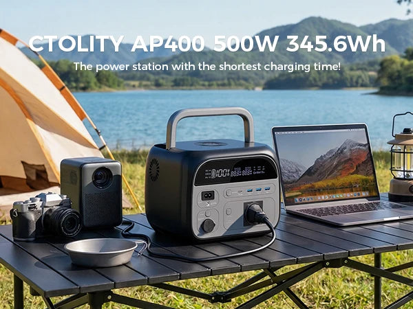 A black portable power station is shown on a wooden table next to a laptop and camera, set outdoors by a lake.