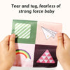 Hands are tearing and tugging a sensory tissue box baby toy with crinkle scarves featuring various colors and shapes.