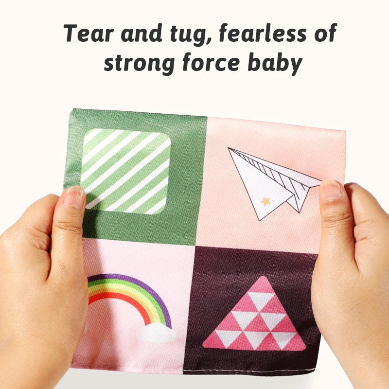 Hands are tearing and tugging a sensory tissue box baby toy with crinkle scarves featuring various colors and shapes.