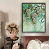A framed painting featuring green grapes and white pearls on a branch against a light green background.