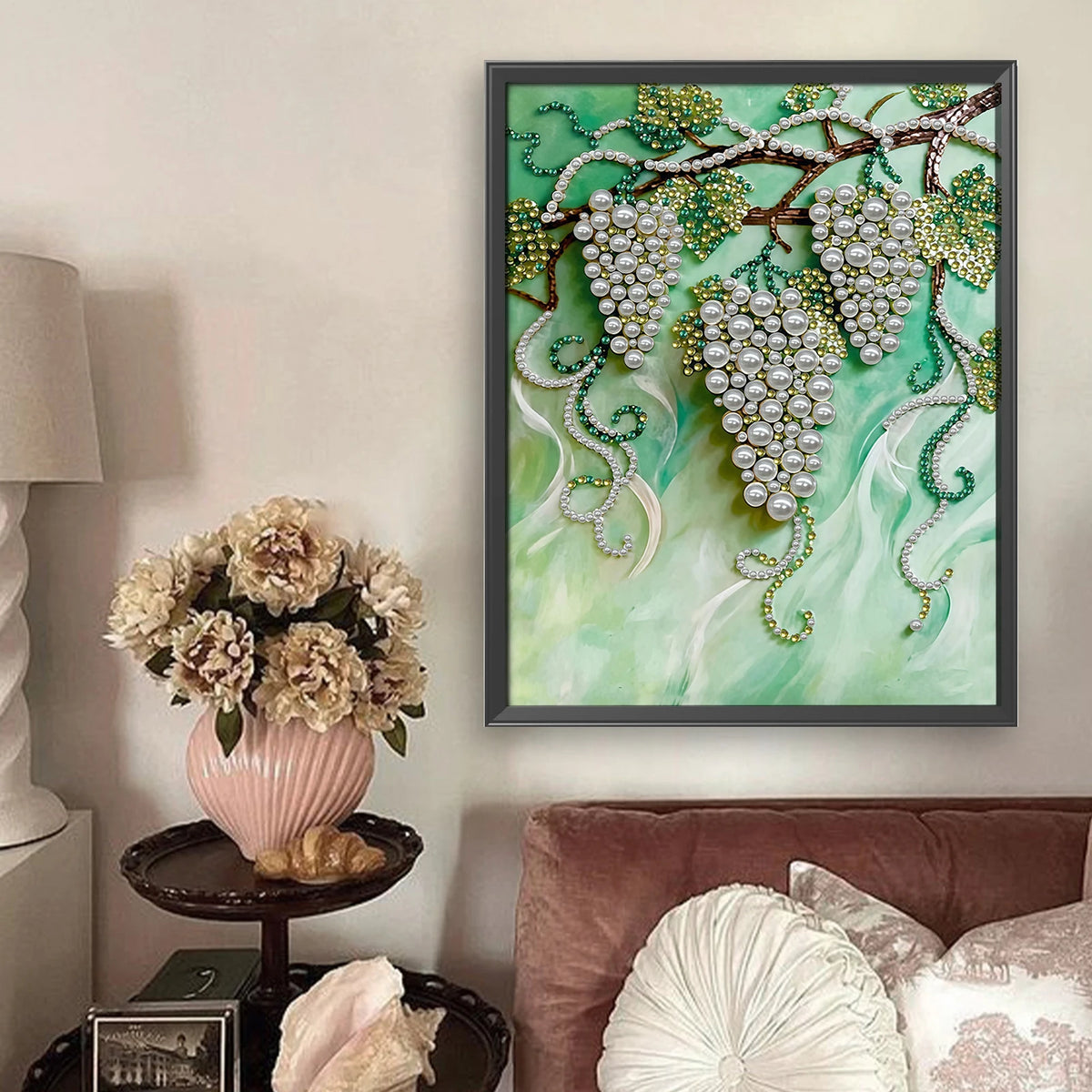 A framed painting featuring green grapes and white pearls on a branch against a light green background.