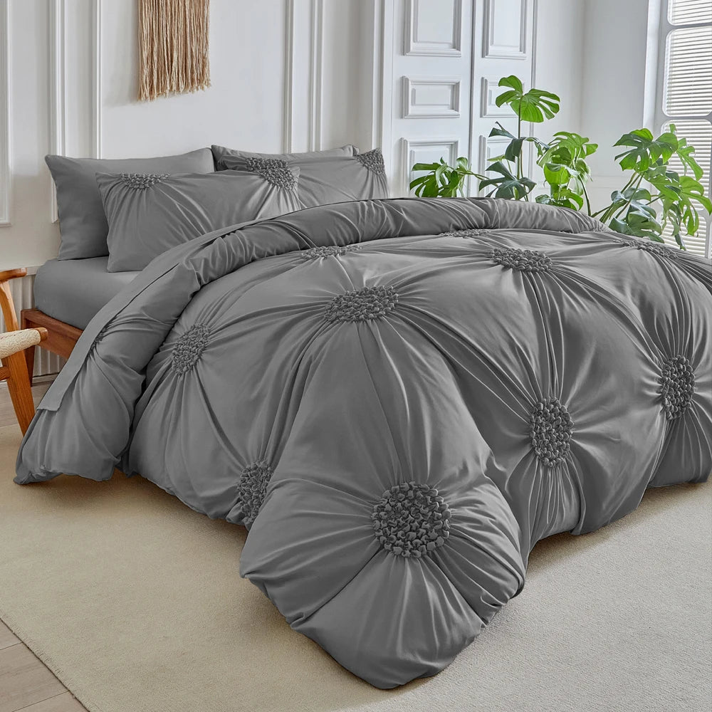 A gray three-dimensional pleated floral duvet cover set displayed on a bed with white trim and greenery.
