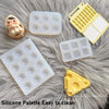 A collection of yellow and white silicone paint palette trays and tools resting on a fluffy gray surface.