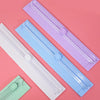 Three portable paper cutters or trimmers in white, light blue, and purple lying on a pink surface.