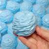 Eine Hand hält einen hellblauen, quetschbaren Stressball-Spielzeug inmitten vieler ähnlicher Spielzeuge.
