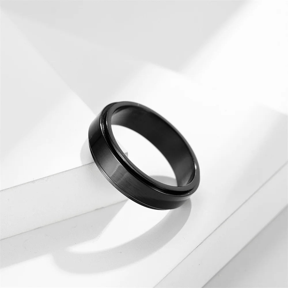 A black stainless steel anxiety spinner ring resting on a white surface with soft lighting.