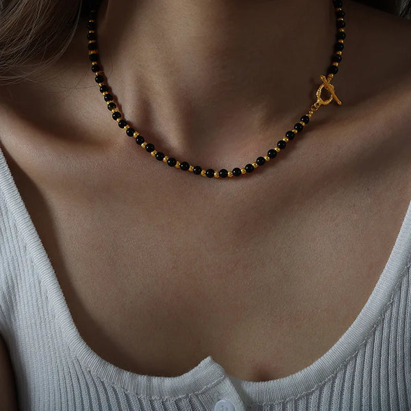 Rapproché d'un collier de perles d'agate vintage avec des accents dorés porté autour du cou sur un fond neutre.