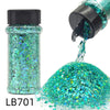A glass bottle of holographic teal glitter nail mix with a black shaker top and a pile of loose glitter.