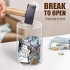 A hand uses a wooden tool to open a clear acrylic piggy bank filled with various coins and bills.