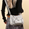 A light gray leather tote bag with a tan strap is carried by a person wearing a black top and a gray skirt.