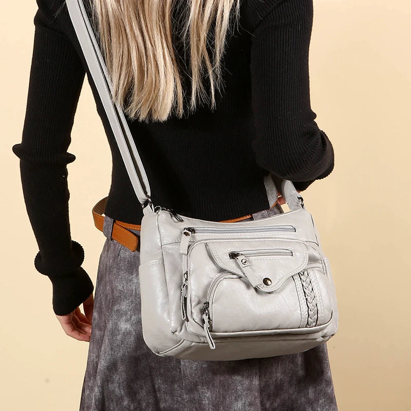 A light gray leather tote bag with a tan strap is carried by a person wearing a black top and a gray skirt.