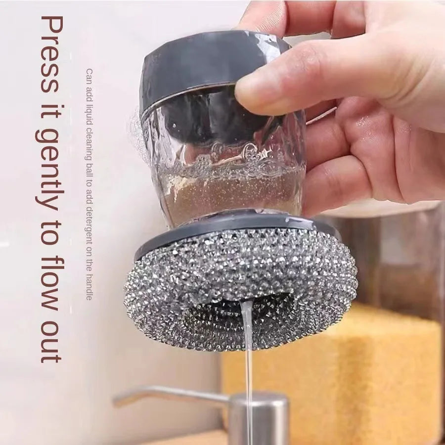 A hand is pressing a dish brush with a built-in soap dispenser to allow liquid detergent to flow out.
