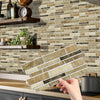 A hand is placing peel and stick waterproof tile stickers on a kitchen backsplash made of stacked rectangular tiles.