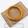 A coil of gold-colored anodized aluminum jewelry wire resting on a wooden board.