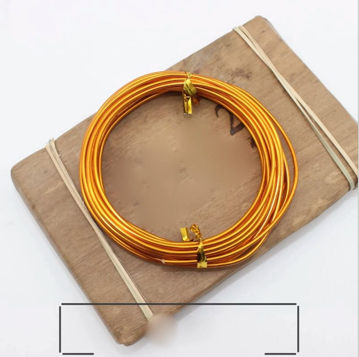 A coil of gold-colored anodized aluminum jewelry wire resting on a wooden board.