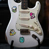 A white electric guitar features several colorful skull stickers on the body and neck.