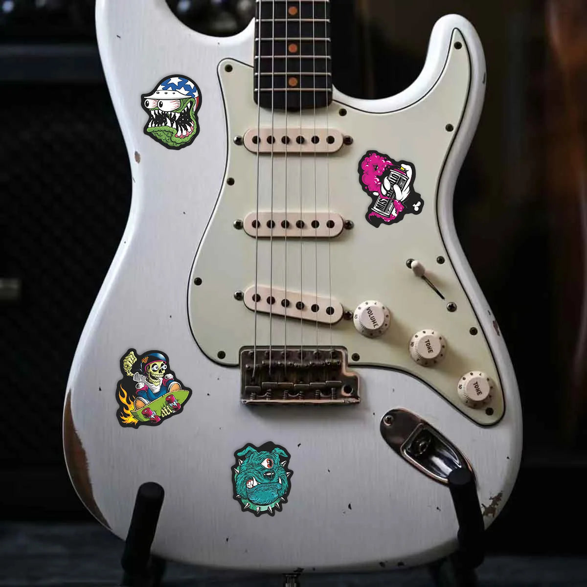 A white electric guitar features several colorful skull stickers on the body and neck.