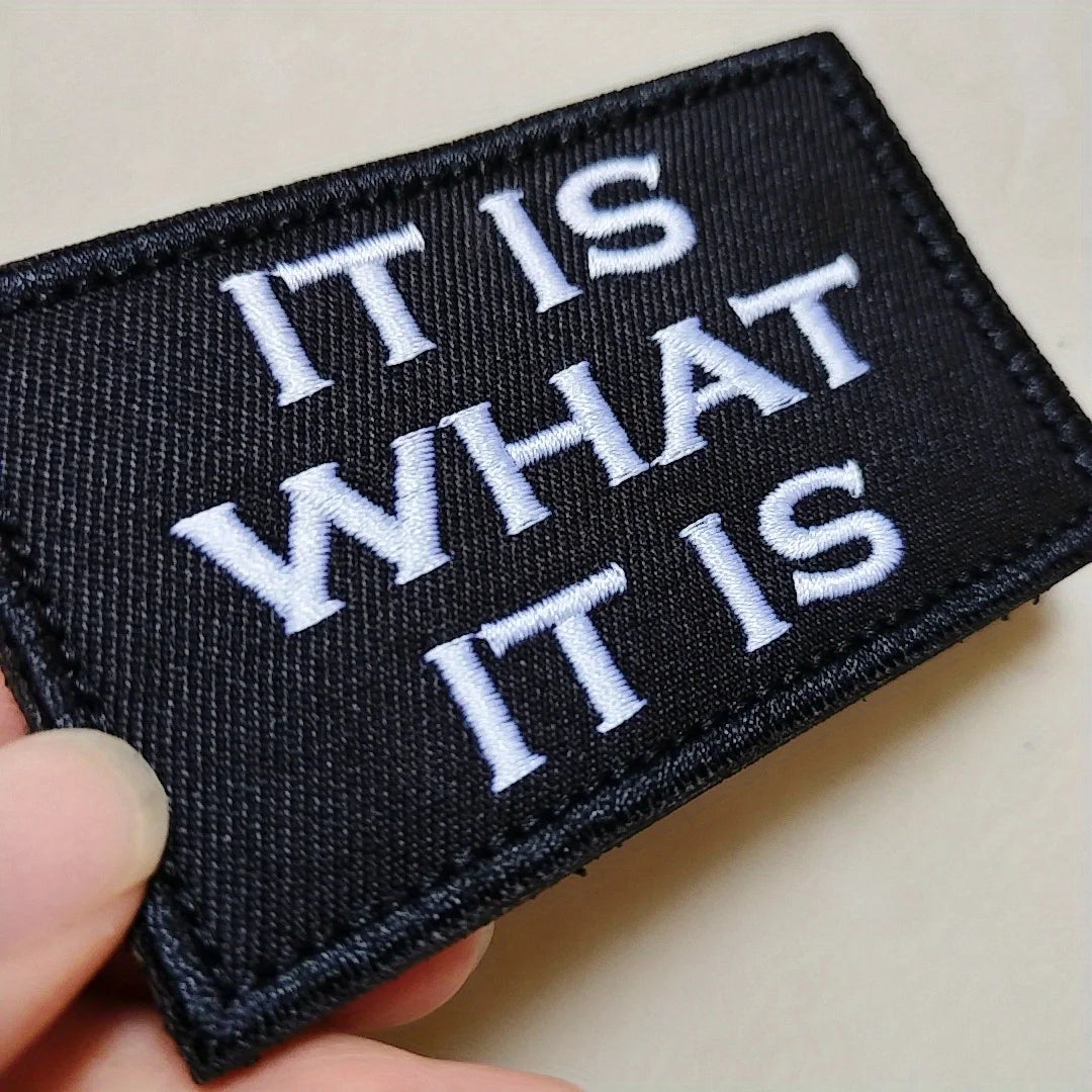 Black embroidered tactical morale patch with white text reading IT IS WHAT IT IS