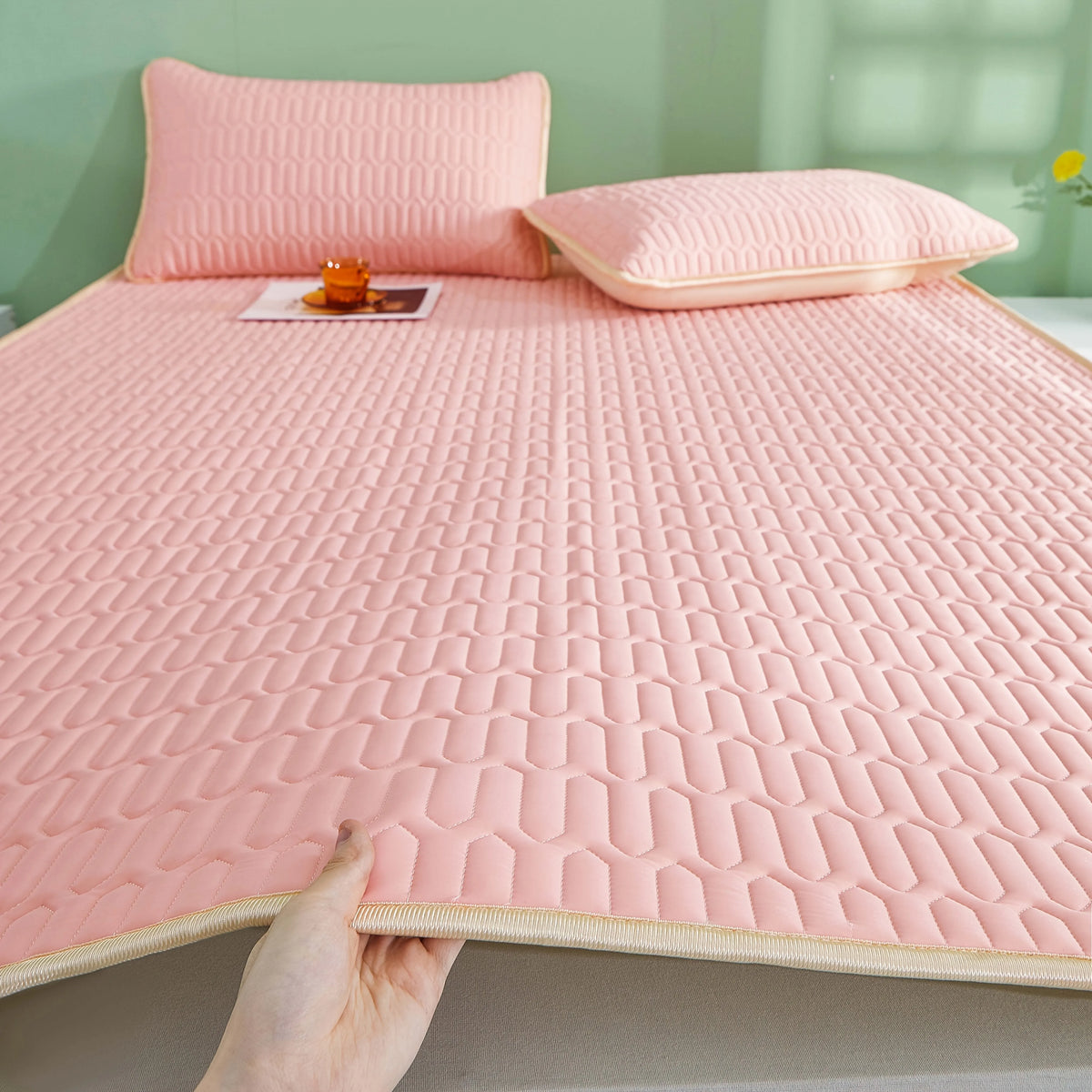 Almohada de enfriamiento rosa transpirable con textura acolchada y almohadas a juego en una cama.