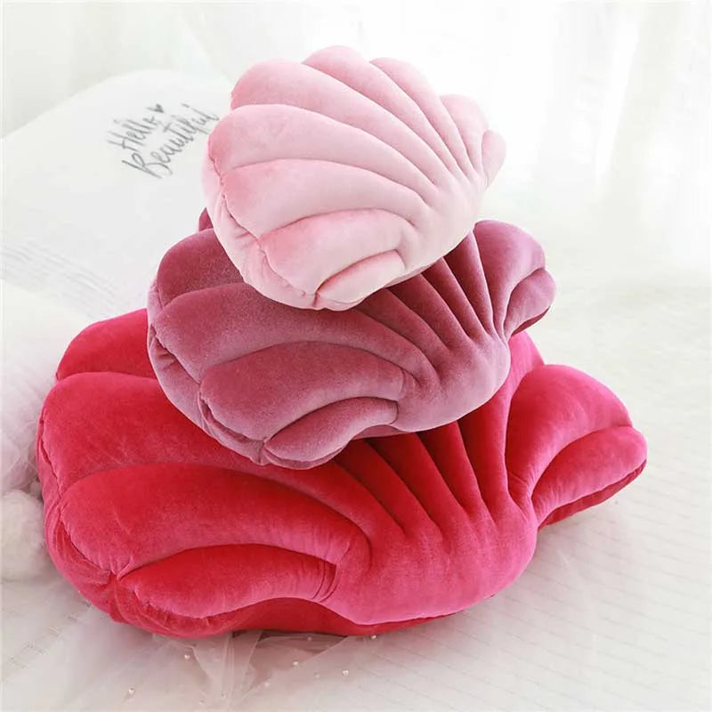 A stack of pink and red velvet shell print throw pillows on a white surface.