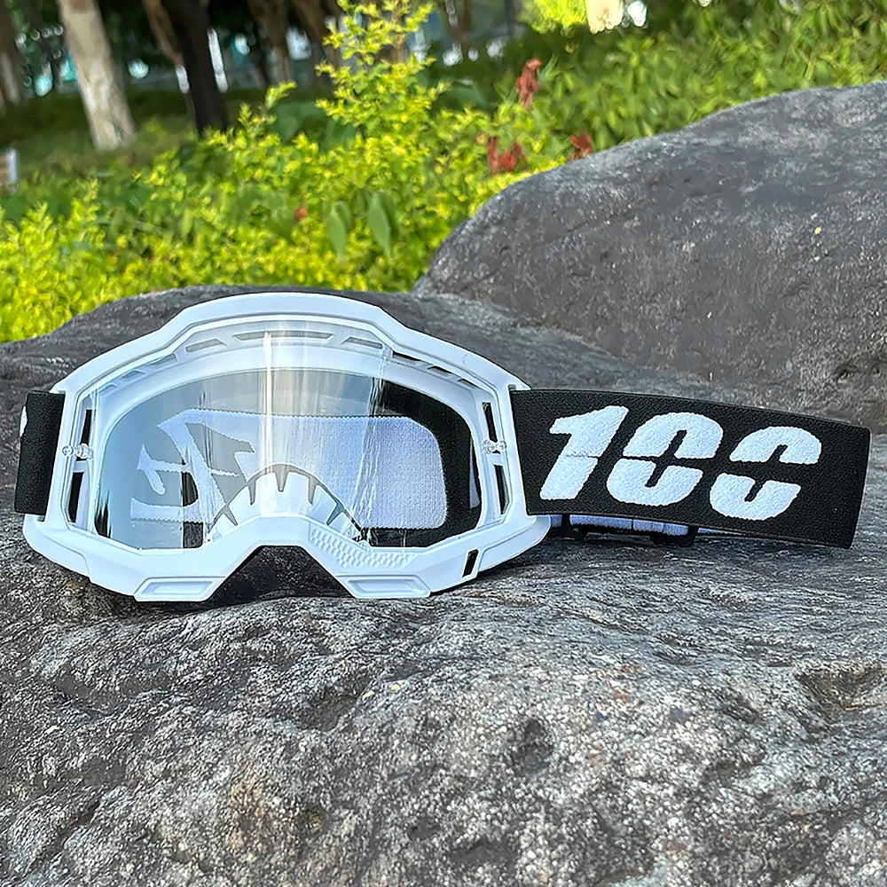 White motocross goggles with black strap resting on a gray rock.