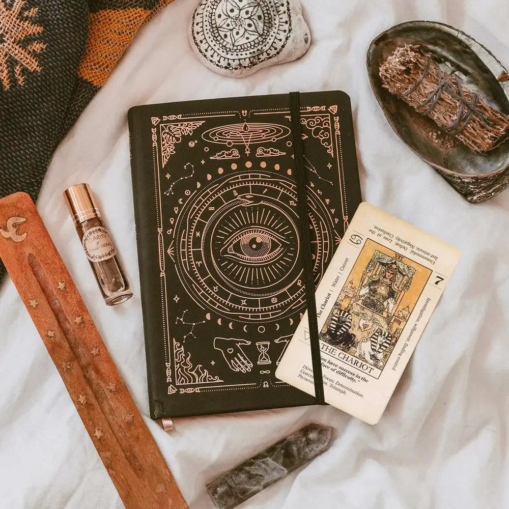 An antiqued tarot deck with meanings on cards is displayed on a white surface next to a wooden stick and other spiritual item