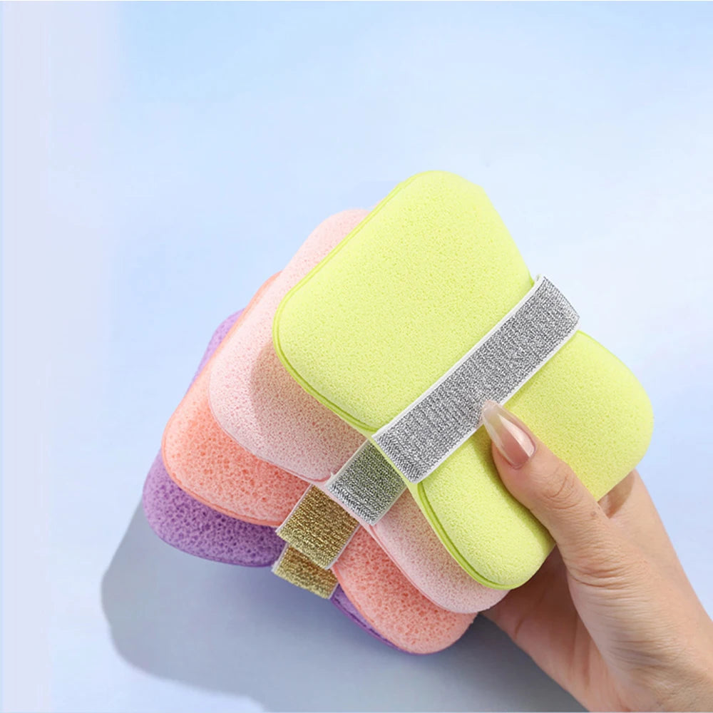 A hand holds a colorful foaming soap saver bag with exfoliating mesh in various pastel colors against a light blue background